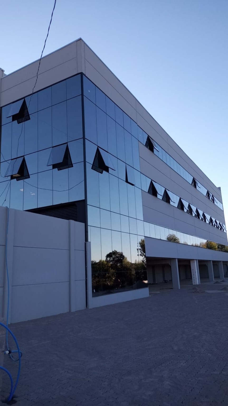 Fachada tipo pele de vidro com vidro refletivo e perfis de alumínio, com acabamento e fixações do sistema.